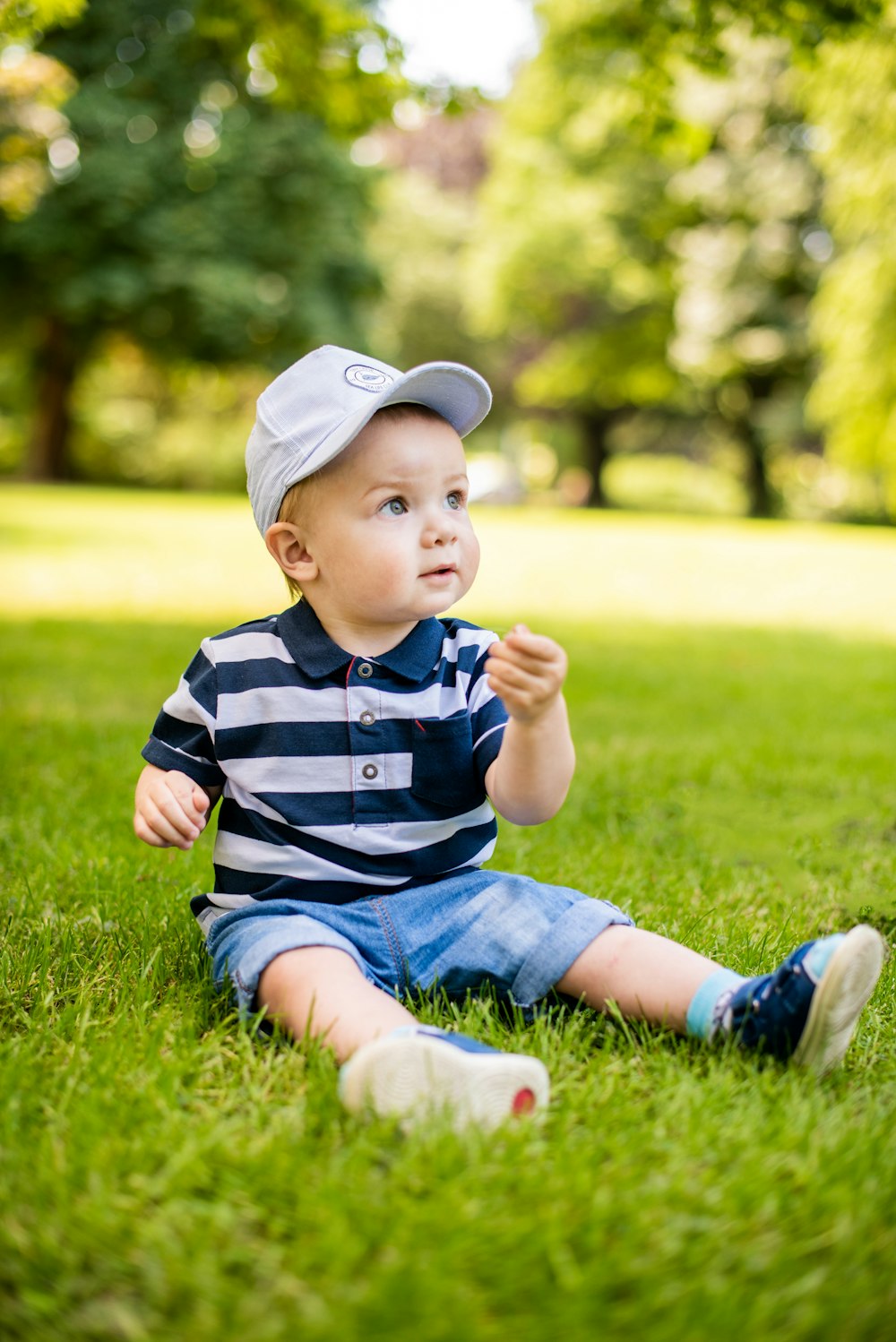 boy in blue and white stripe polo shirt and blue denim shorts sitting on green grass