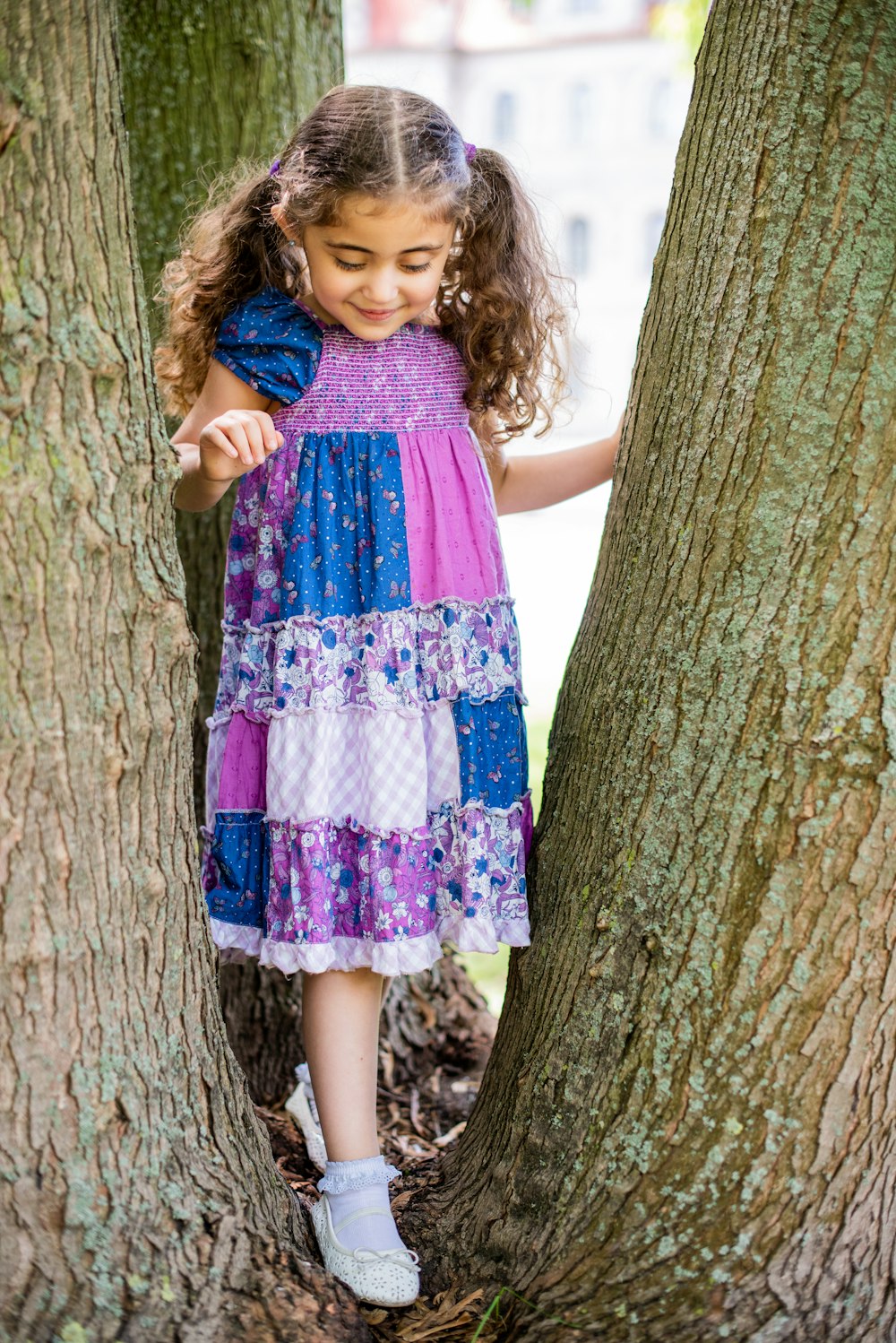 Mädchen in lila und weißem Blumenkleid neben Baum