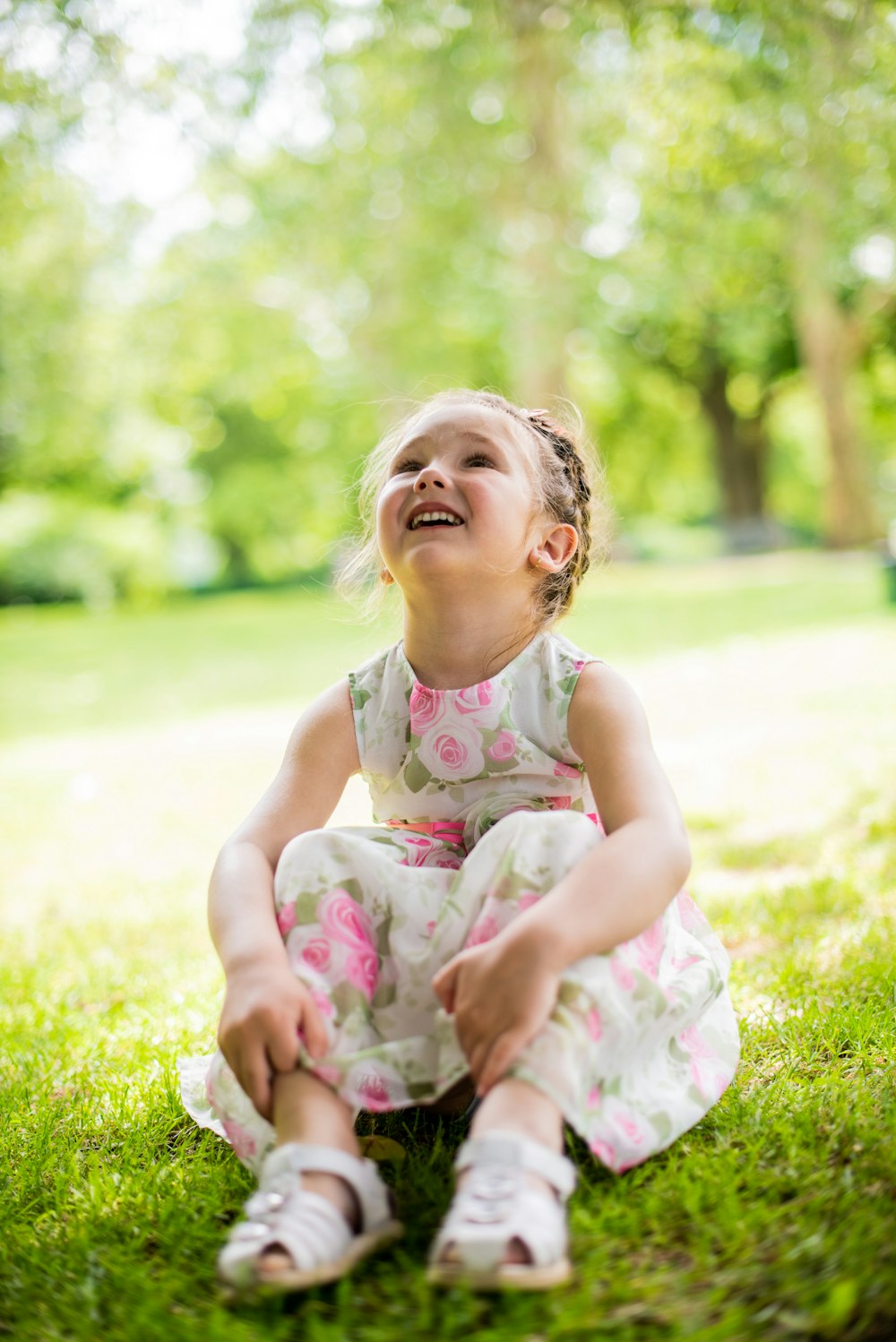 girl in white and pink floral tank dress sitting on green grass field during daytime