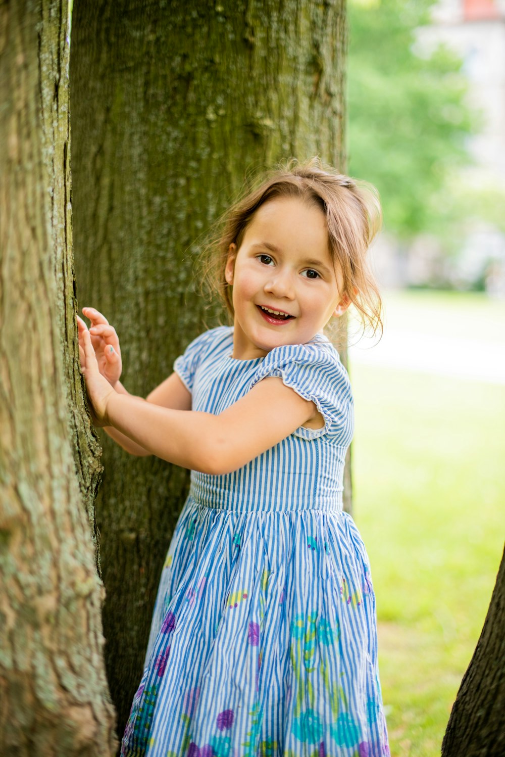 girl in blue and white polka dot dress standing beside brown tree during daytime