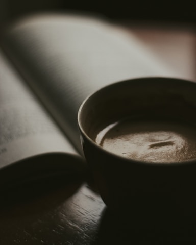 Cozy coffee shop corner with a steaming cup of coffee and an open book on a wooden table.