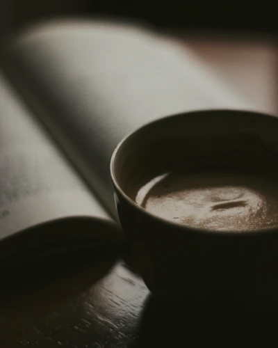 A cozy café corner with amber lights glowing through rain-speckled windows, shelves of fantasy novels, and a steaming cup of coffee beside an open Kindle.