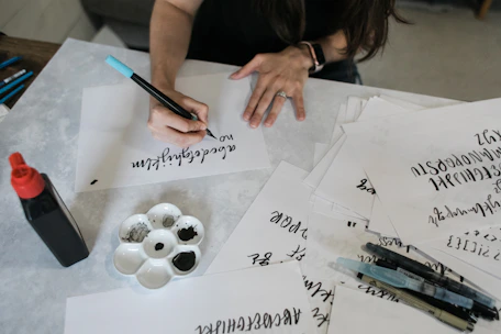 A student practicing calligraphy with a fountain pen, surrounded by ink cartridges and paper