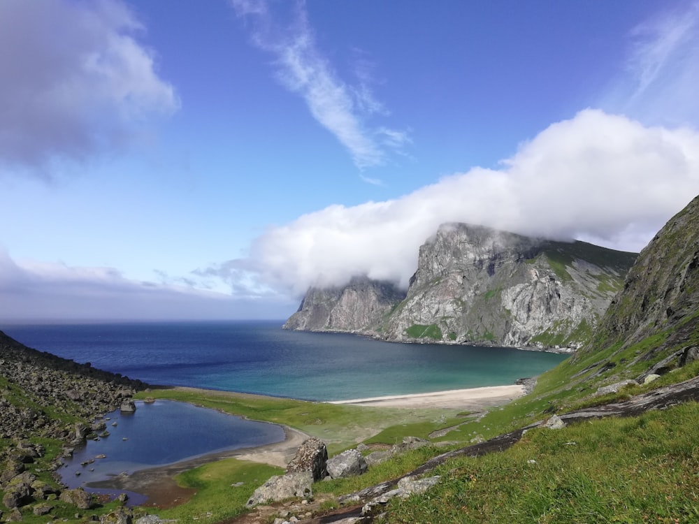 green and gray mountain beside body of water under blue sky during daytime