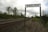 A railway track extends into the distance bordered by grassy areas and trees under a cloudy sky. A signpost prominently displays the word 'ENGLISH' above the tracks.