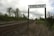 A railway track extends into the distance bordered by grassy areas and trees under a cloudy sky. A signpost prominently displays the word 'ENGLISH' above the tracks.