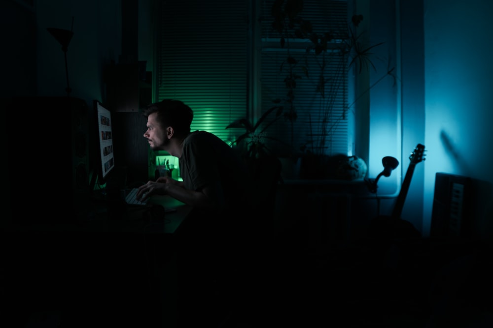 man in black shirt sitting on chair using laptop computer