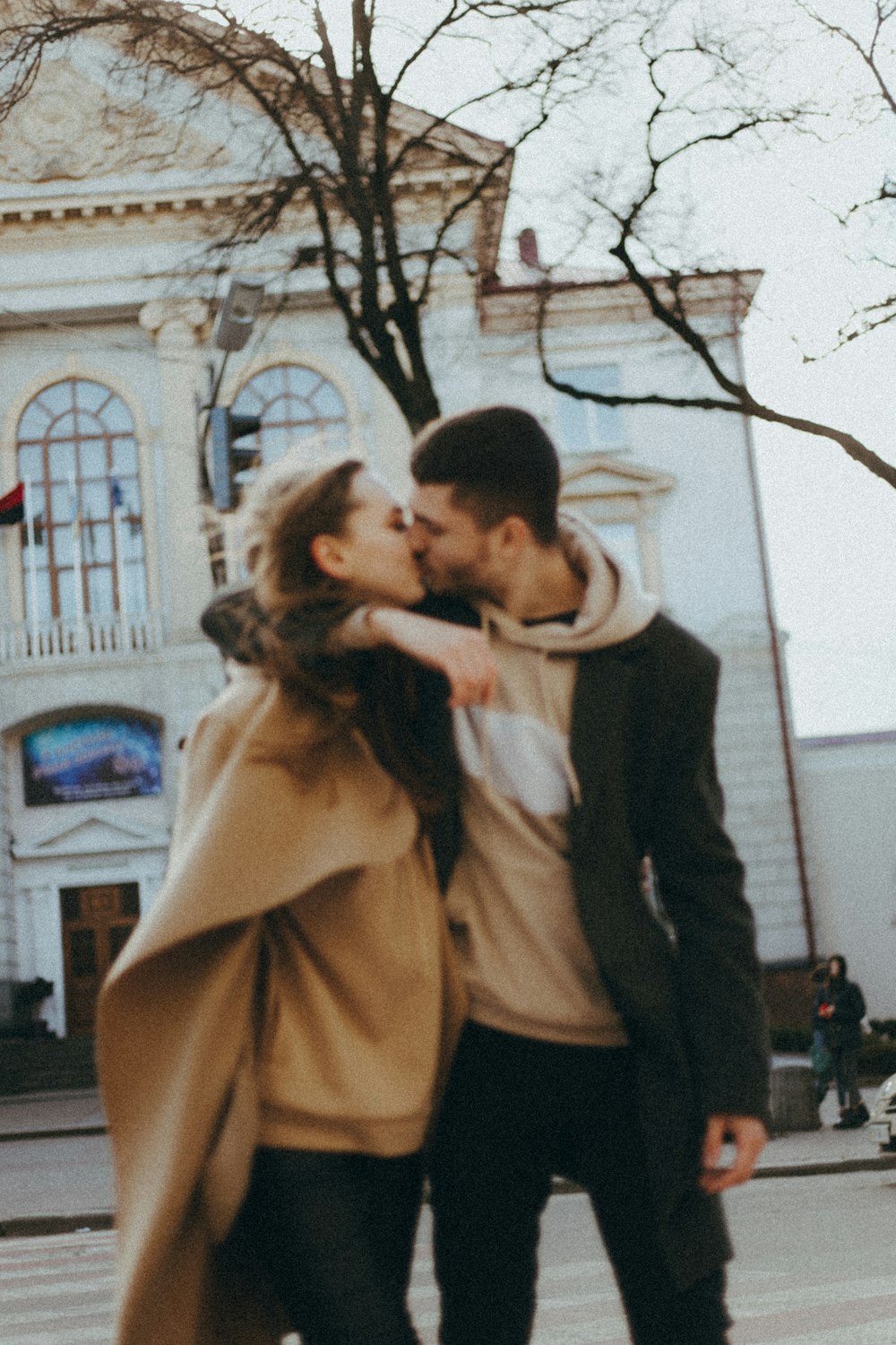 uomo in abito nero che bacia la donna in cappotto marrone