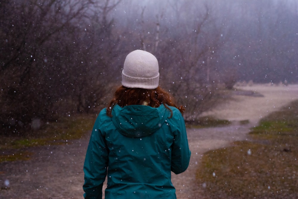 person in green jacket and white knit cap standing on road during daytime