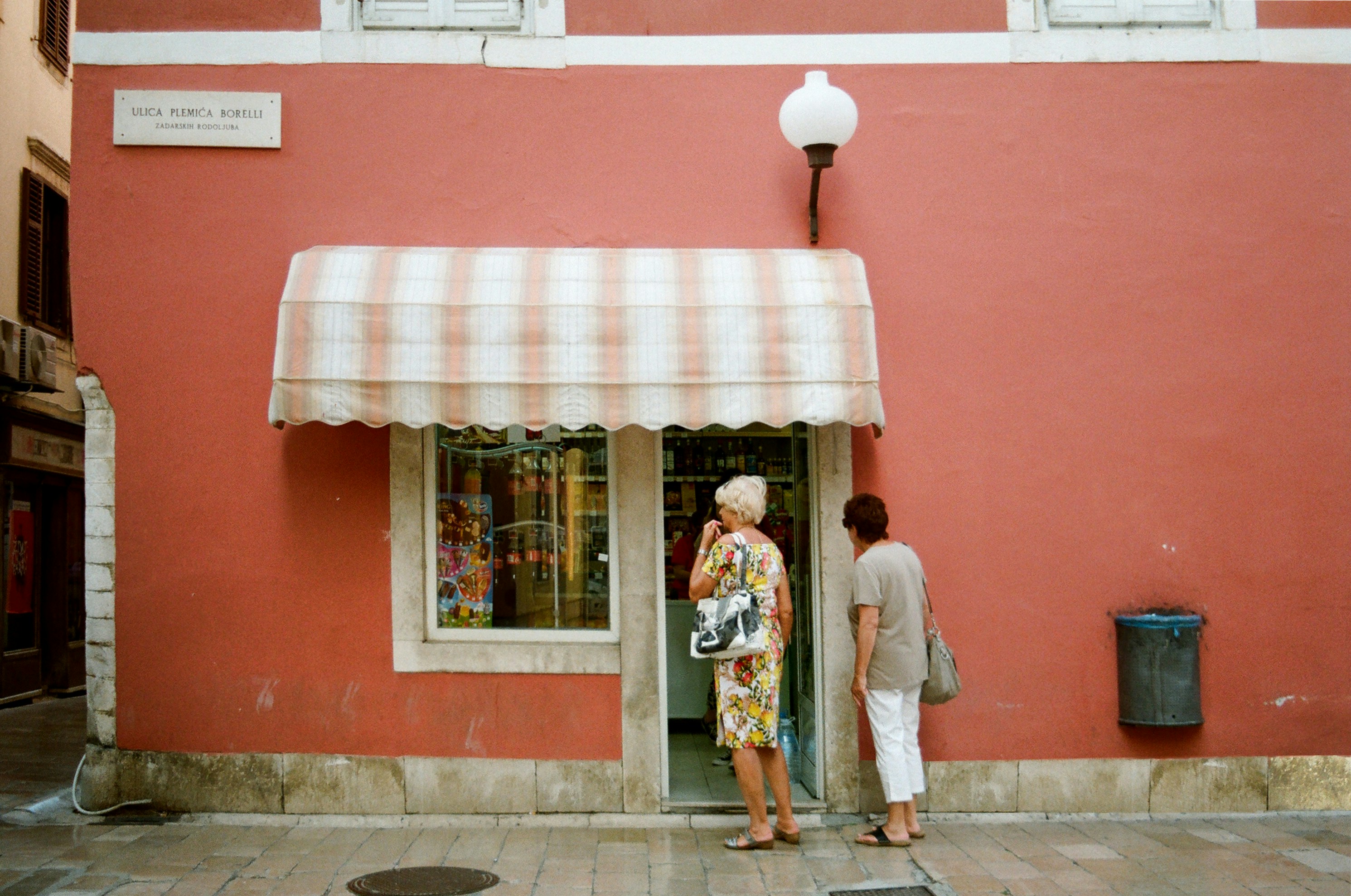 Two people at a red shopfront with a striped awning