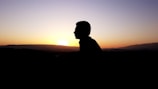 A silhouette of a person watching the sun set behind distant mountains