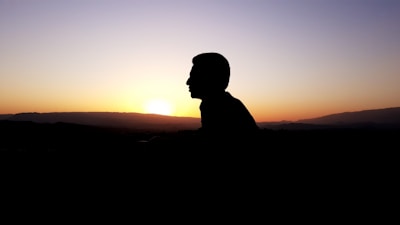 A silhouette of a person watching the sun set behind distant mountains