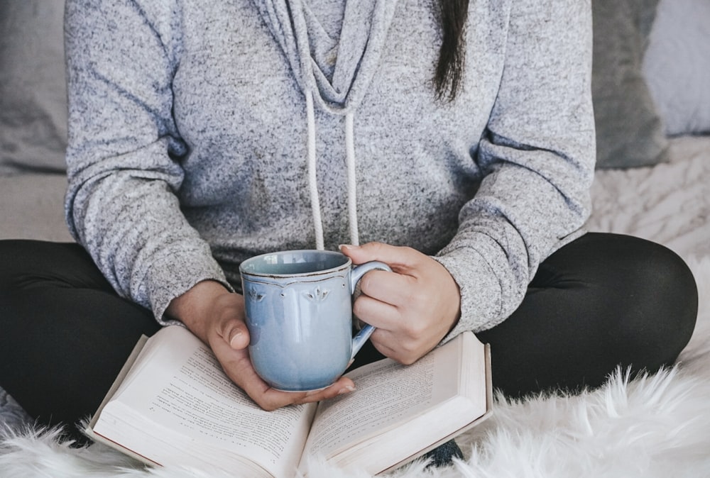 person in gray sweater holding white ceramic mug