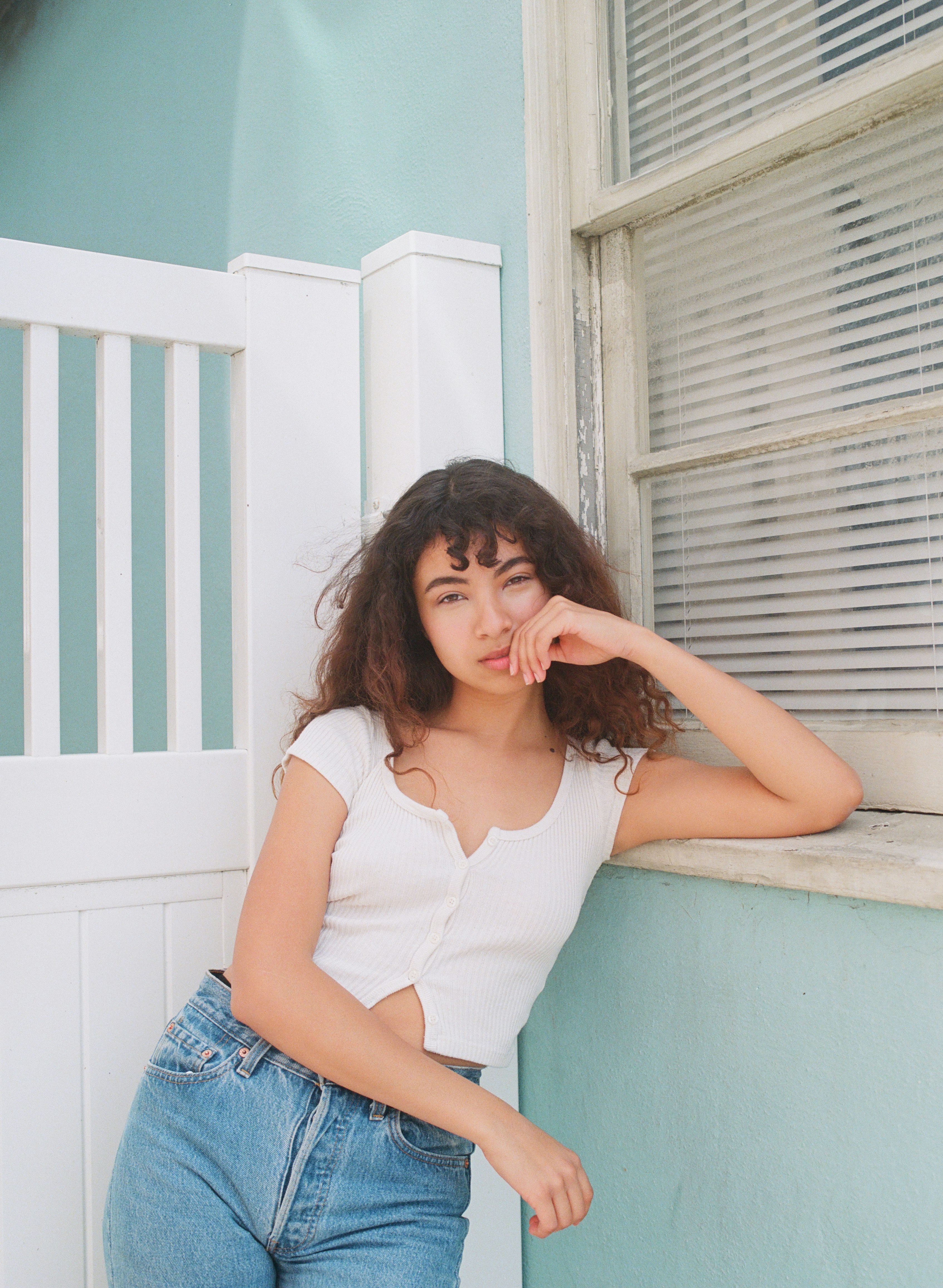 woman in white tank top and blue denim jeans sitting on white concrete wall