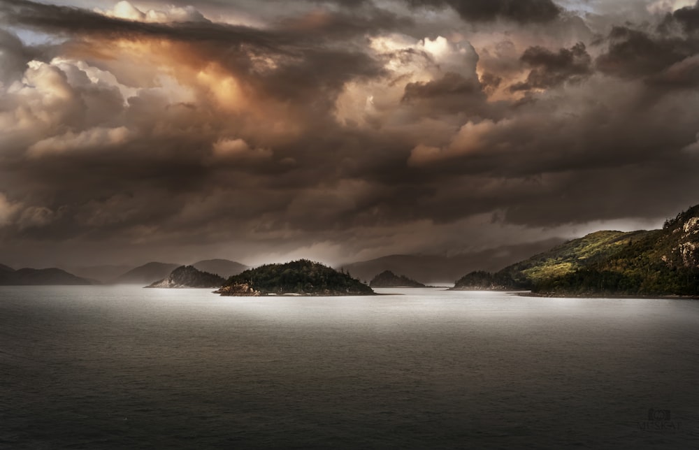 body of water near mountain under cloudy sky during daytime