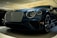 A luxury car is displayed in a showroom with a sleek design and glossy finish. The front grille is prominent, with intricate mesh detailing and chrome accents. The headlights are modern and stylish, and the car's body reflects the showroom lights, adding to its elegance.