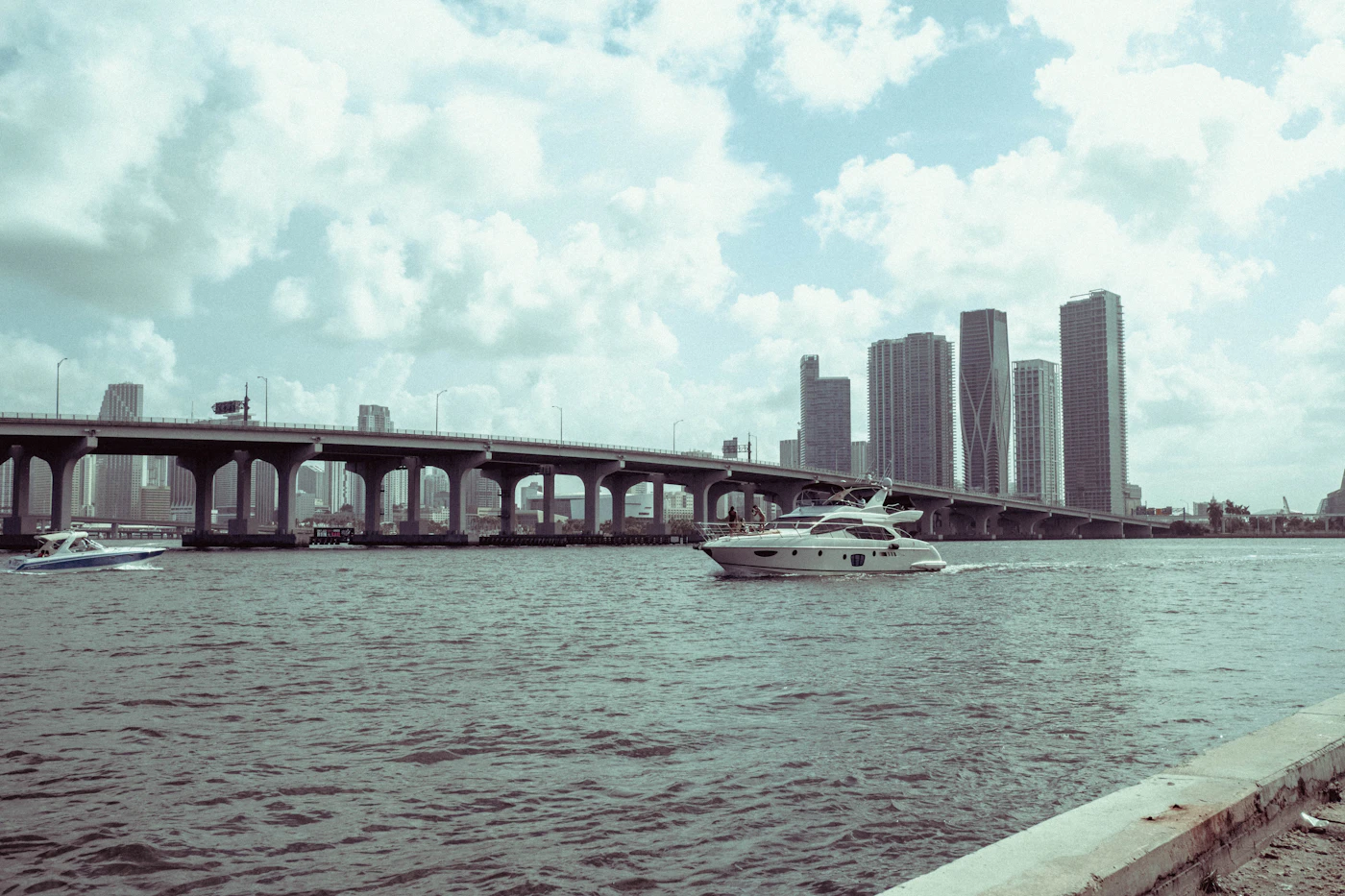 White boat on the water beside a bridge under a cloudy sky
