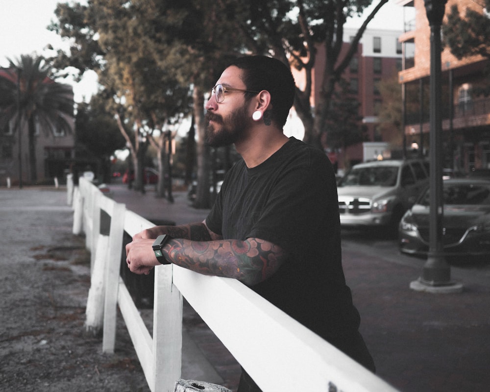 man in black crew neck t-shirt and black sunglasses standing near white wooden fence during