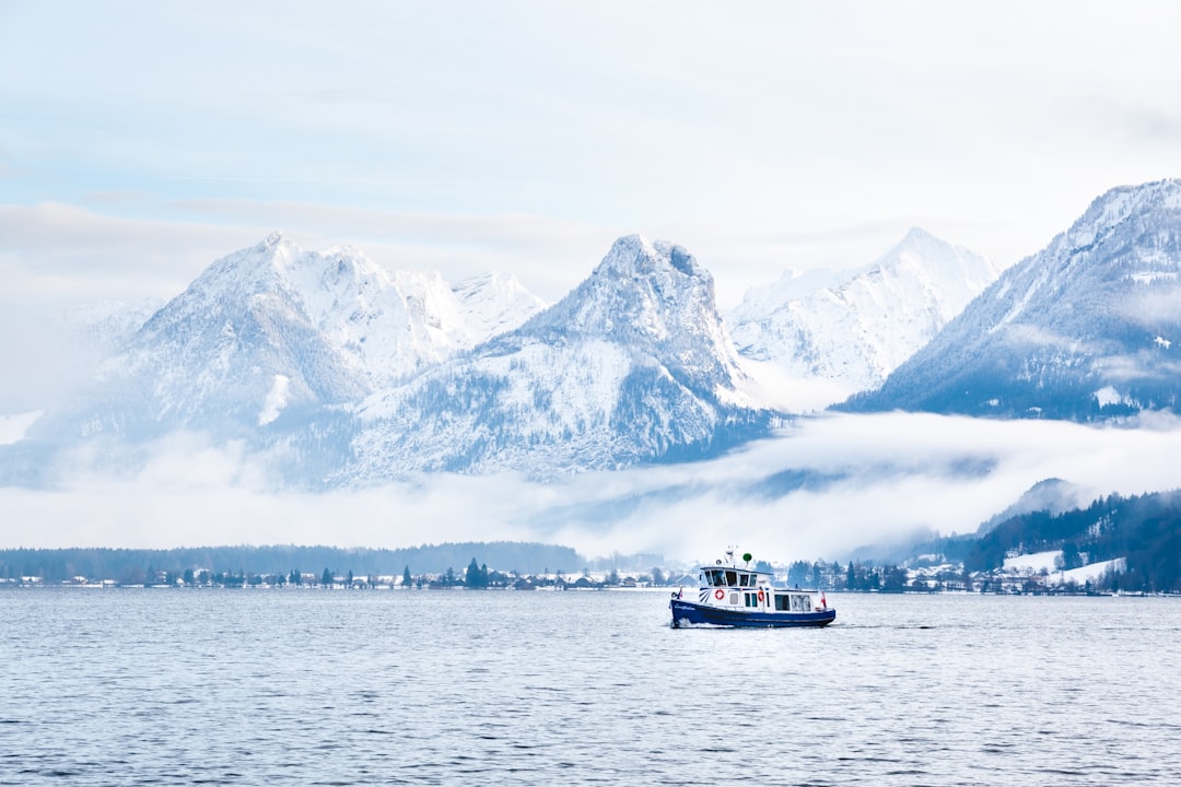 white and black boat on body of water near snow covered mountain during daytime