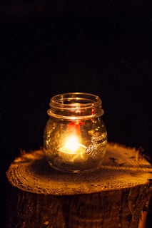 A close-up of a glowing Sunshine Candles jar casting a warm amber light on a wooden table.