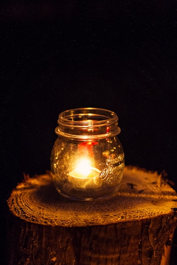 A close-up of a glowing Sunshine Candles jar casting a warm amber light on a wooden table.