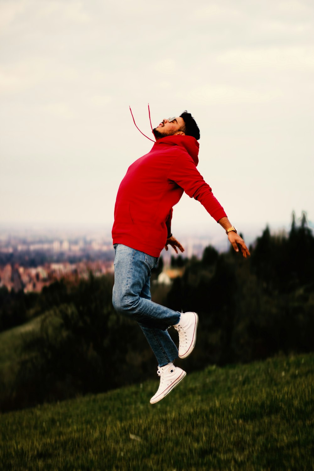 man in red hoodie and blue denim jeans jumping on green grass field during daytime