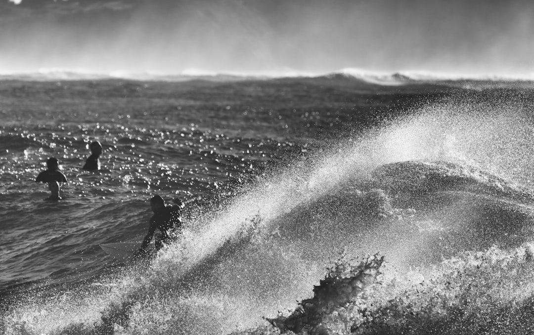 grayscale photo of man surfing on sea waves