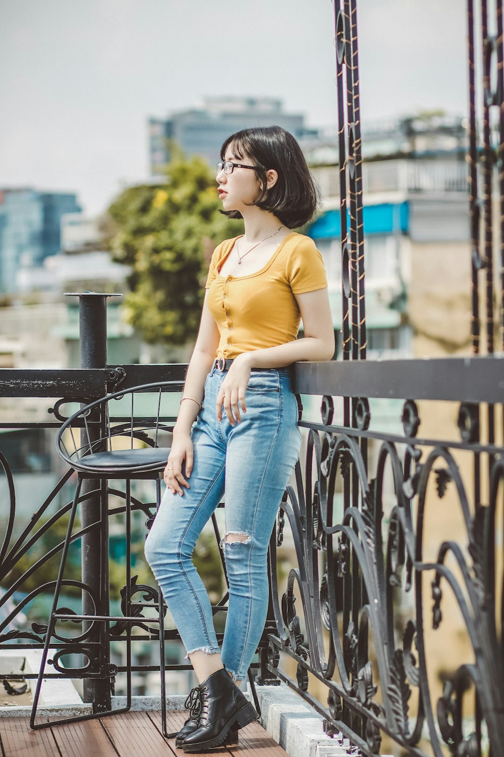 woman in yellow shirt and blue denim jeans leaning on black metal fence during daytime