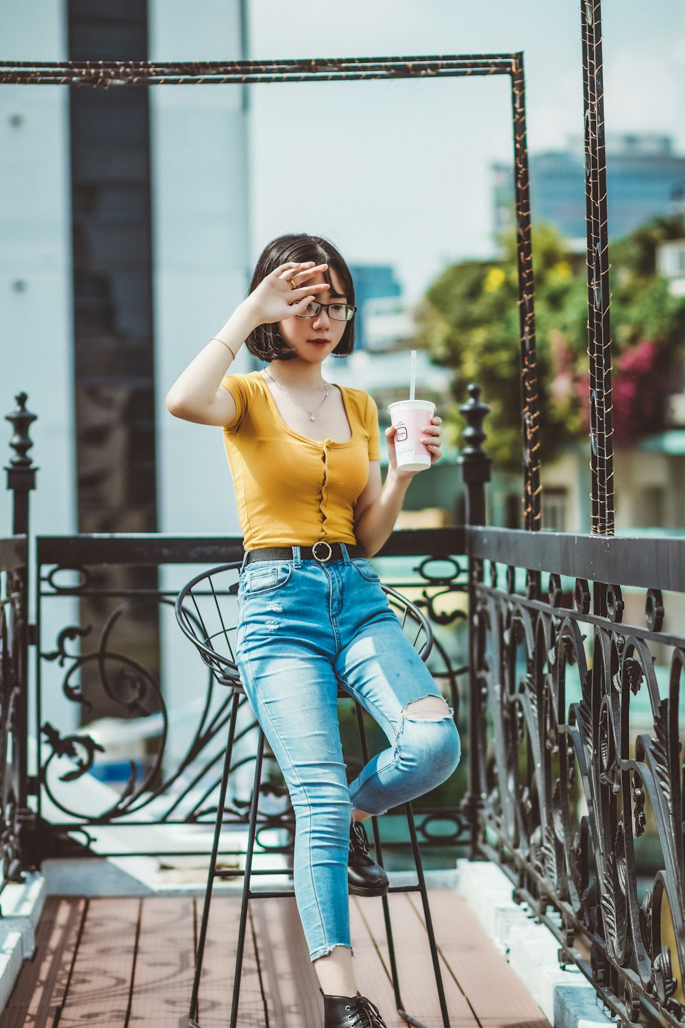 woman in yellow tank top and blue denim jeans sitting on black metal railings during daytime