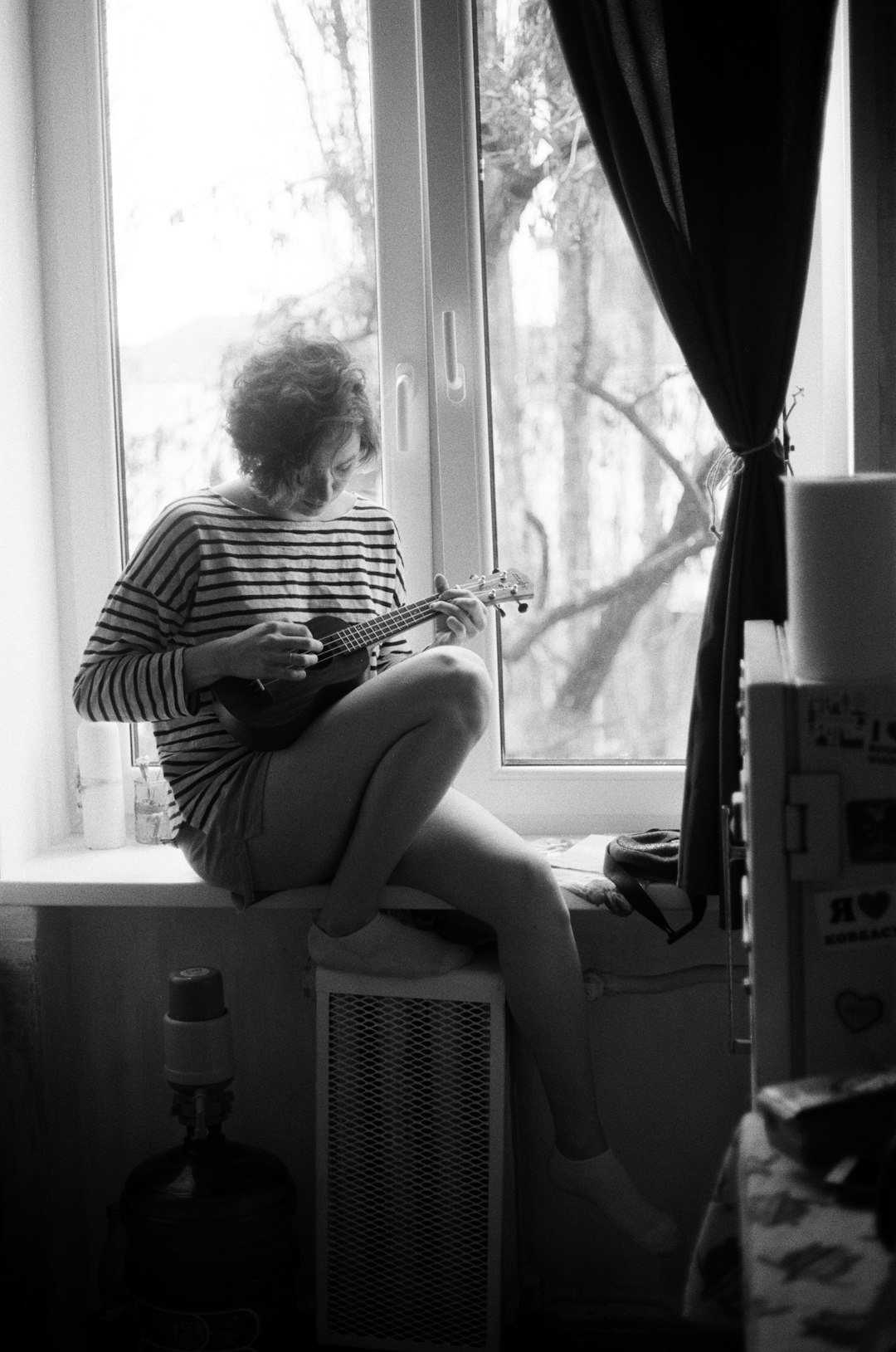 woman playing acoustic guitar sitting on window