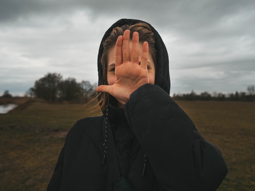 woman in black jacket covering face with her hands