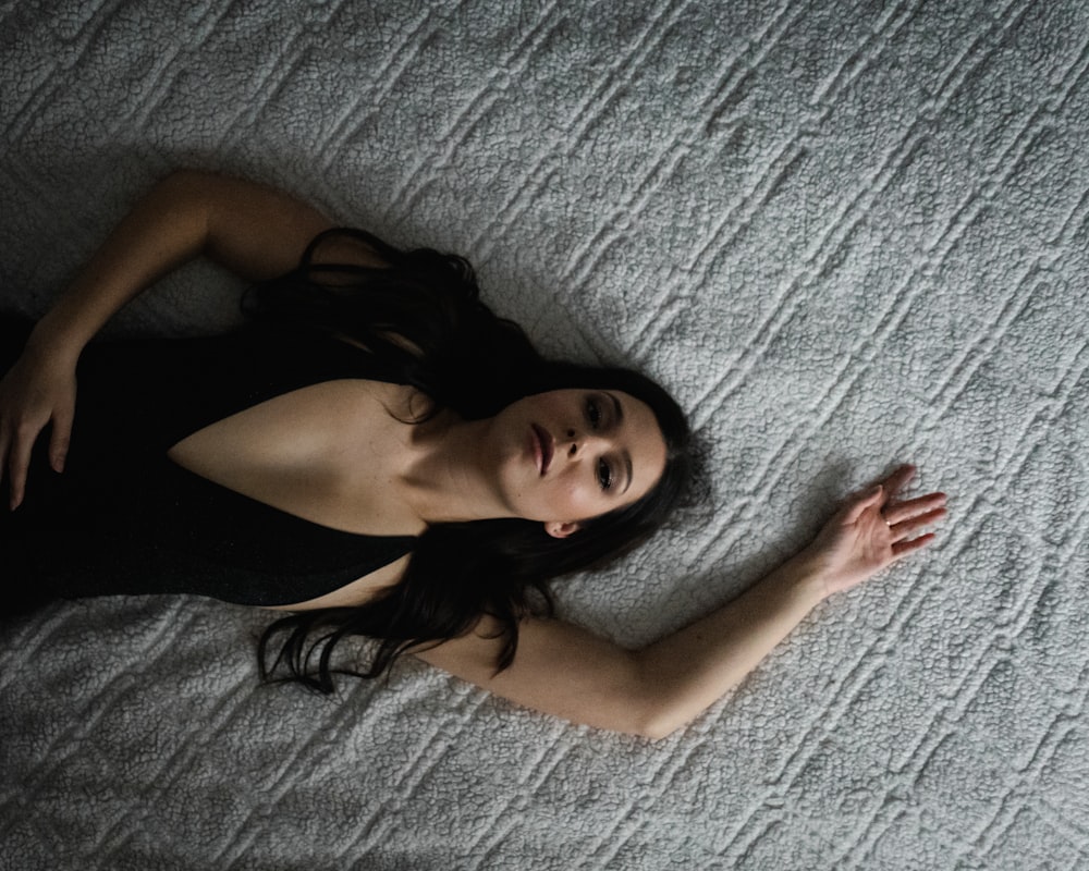 woman in black brassiere lying on grey textile