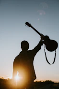 Tony of Tucson standing against a vast desert sunset, guitar slung over his shoulder.