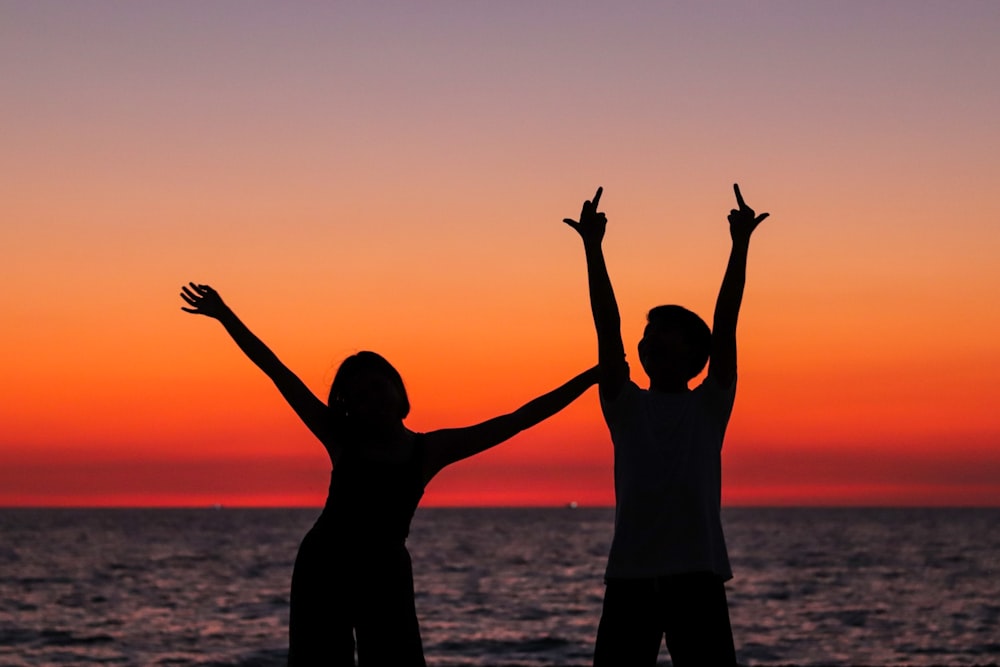 silhouette of 2 person standing on seashore during sunset