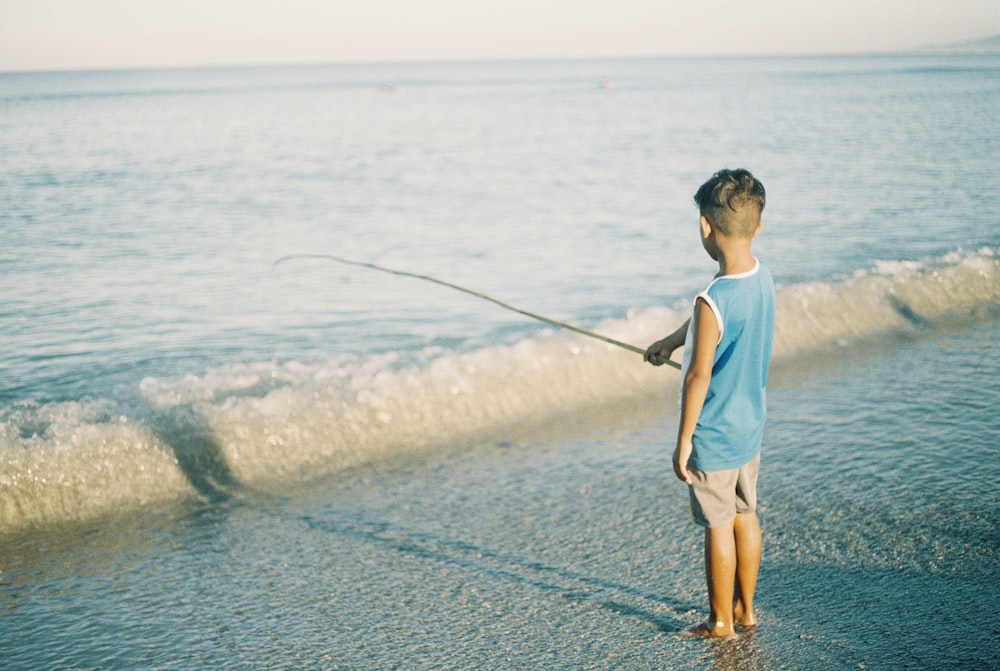 Hombre con camiseta blanca de cuello redondo y pantalones cortos marrones pescando en el mar durante el día