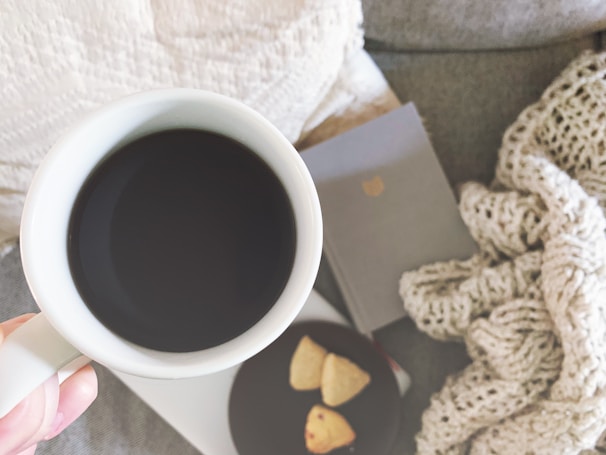 A cozy scene of a hand holding a warm mug of herbal tea next to a small plate of almond cookies.