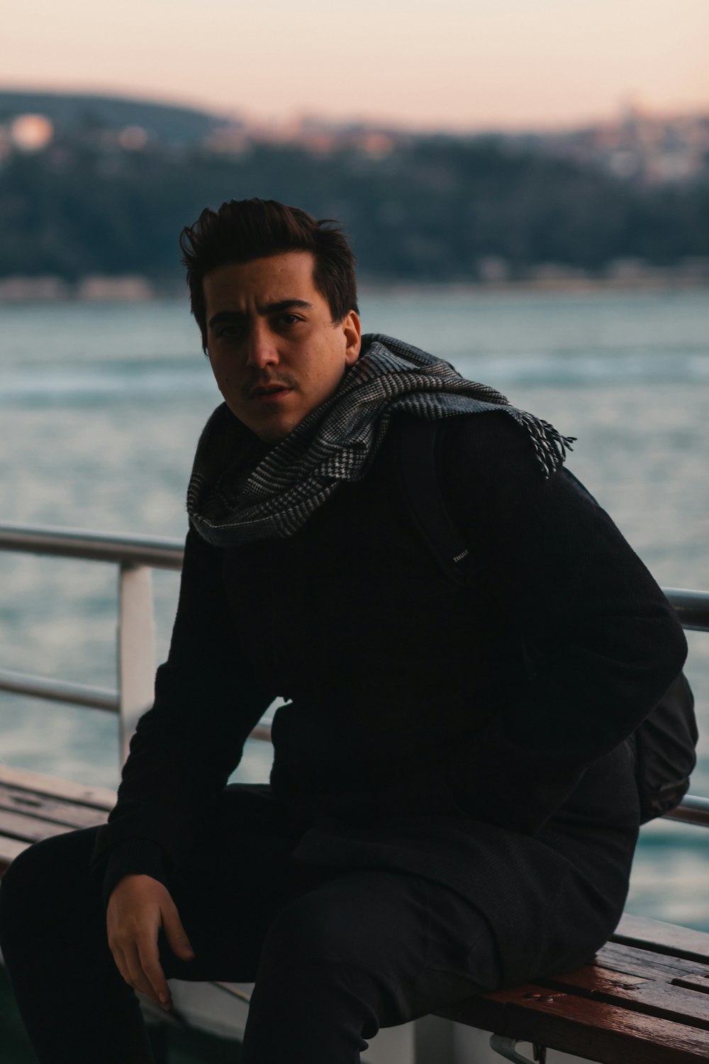 man in black jacket sitting on brown wooden dock during daytime