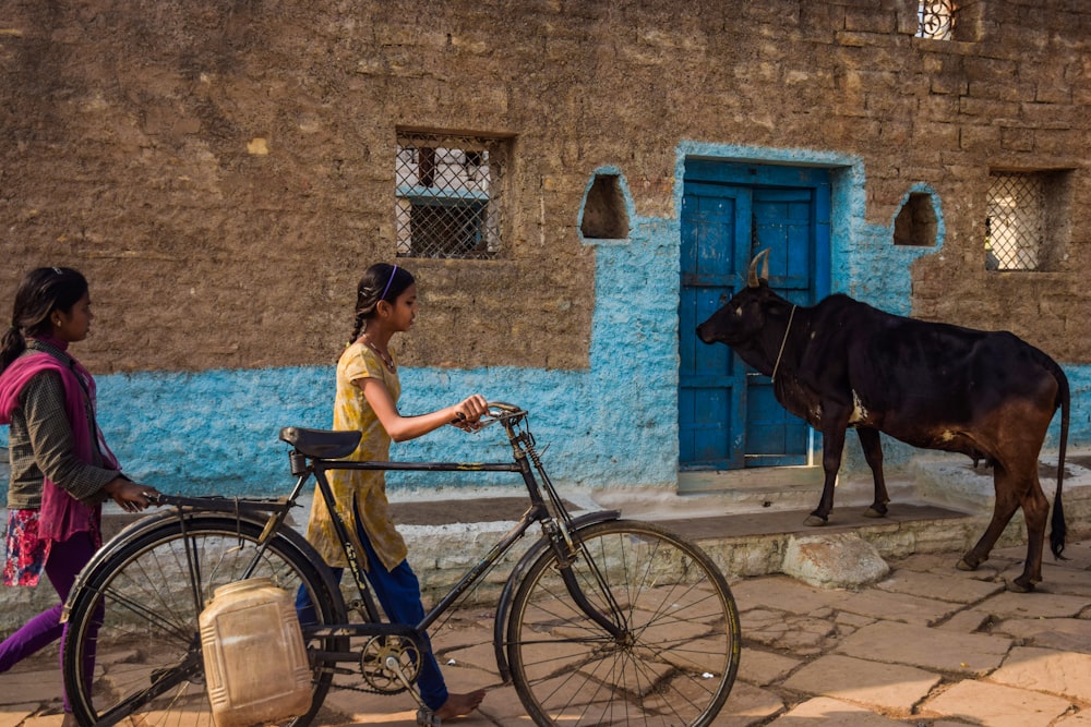 Frau im braunen Hemd fährt tagsüber auf einem schwarzen Fahrrad neben blauem Betongebäude