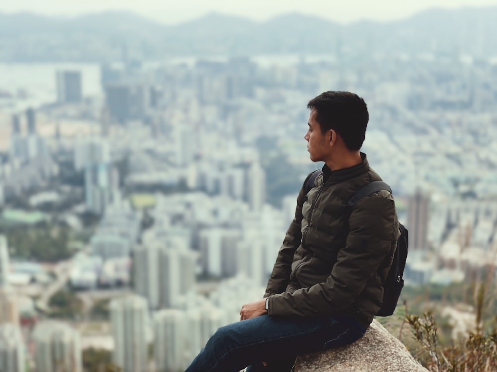 man in brown jacket sitting on rock during daytime