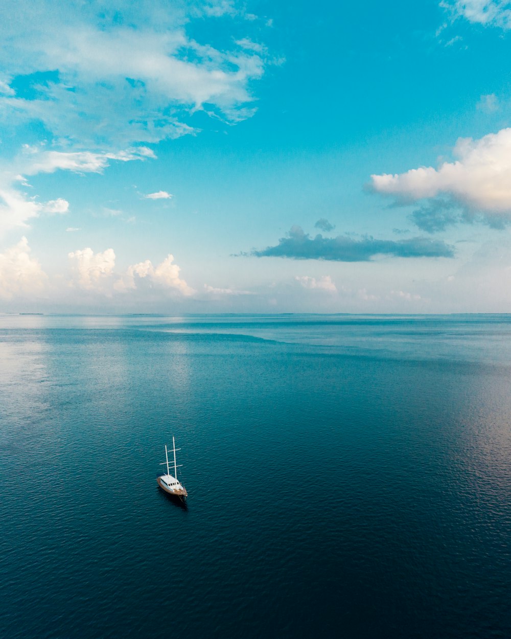 weißes Boot auf blauem Meer unter blauem Himmel und weißen Wolken tagsüber
