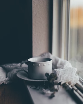 A serene image of a teacup placed on a rainy window sill.