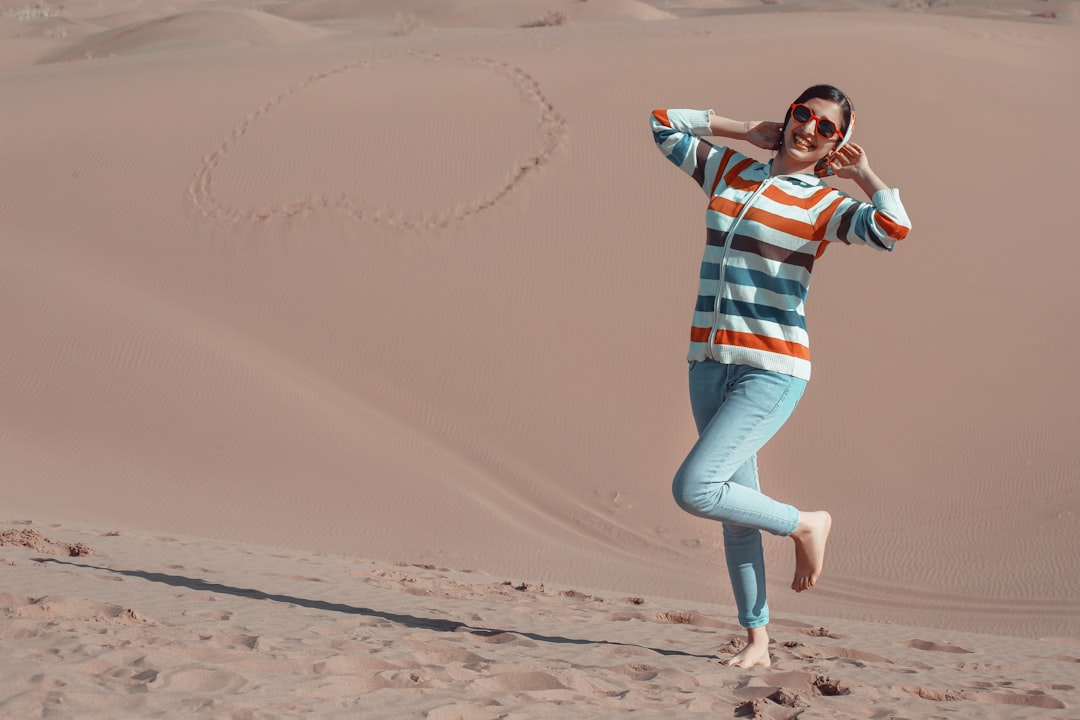 woman in blue and white striped shirt and blue denim jeans jumping on brown sand during