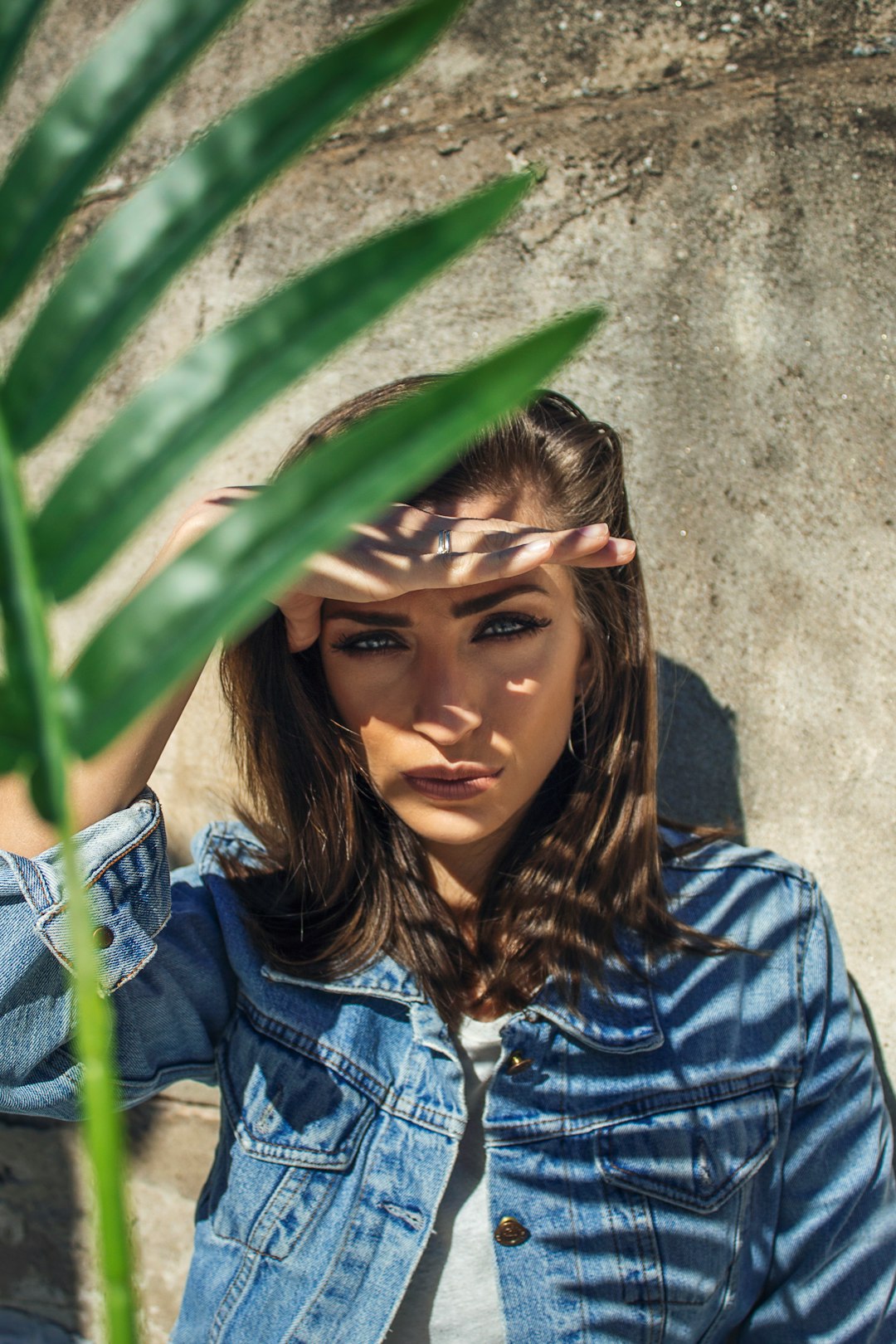 woman in blue denim jacket leaning on green palm tree