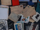 A collection of vintage postcards and envelopes with handwritten addresses is spread out. There are also old photographs and children's illustration cards among the items. Some of the envelopes have vintage stamps affixed. Russian text is visible on several of the items.