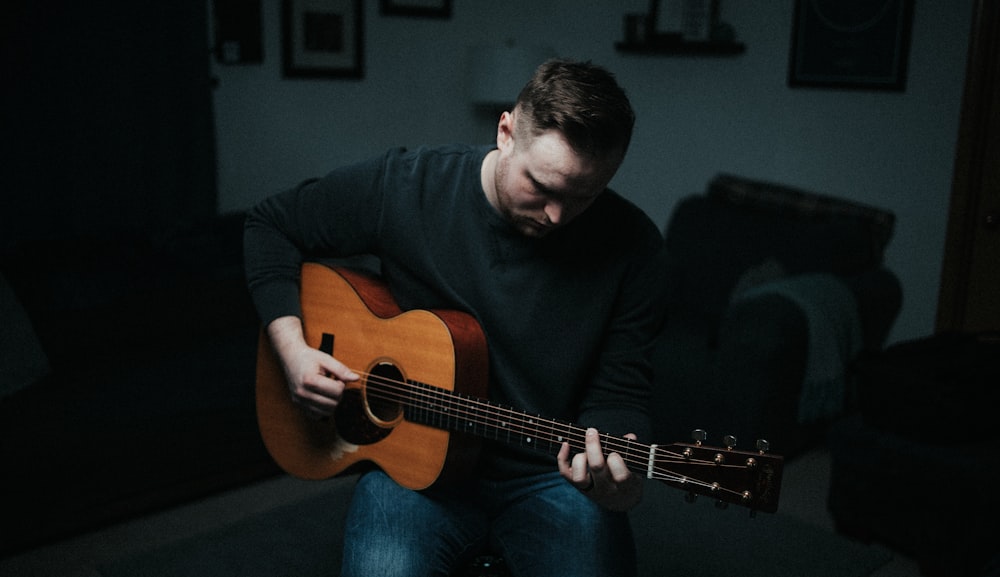 man in black long sleeve shirt playing brown acoustic guitar