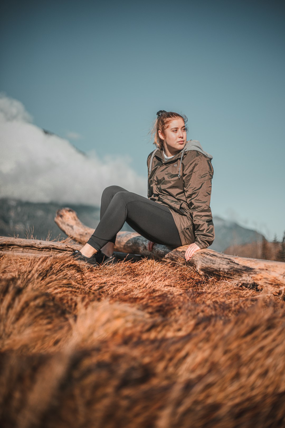 woman in gray jacket and black pants sitting on brown dried grass field