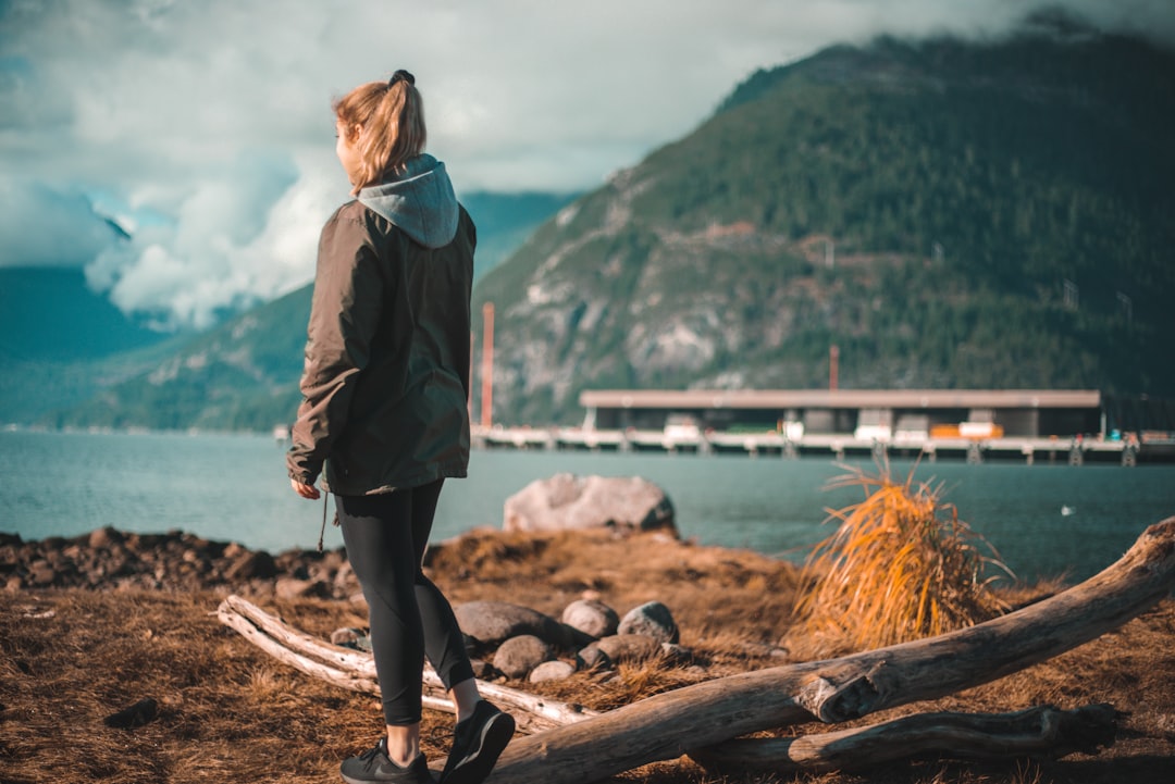 woman in brown coat standing on rock near body of water during daytime