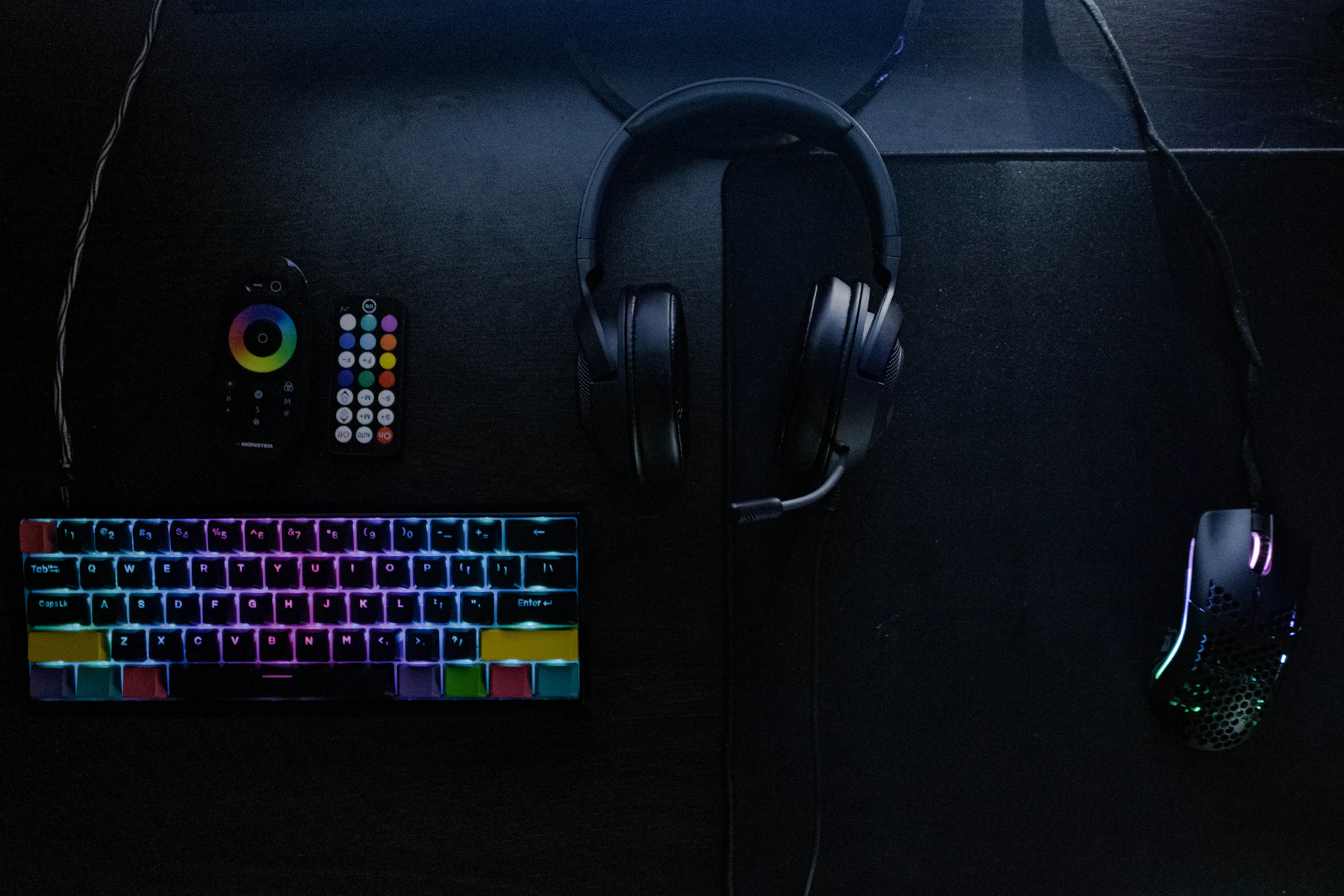Gaming headset beside a compact illuminated mechanical keyboard on a dark gaming desk