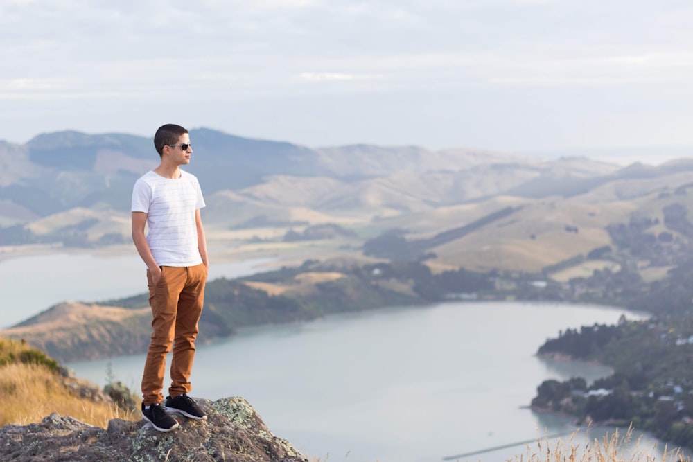 man in white shirt and brown pants standing on rock formation during daytime