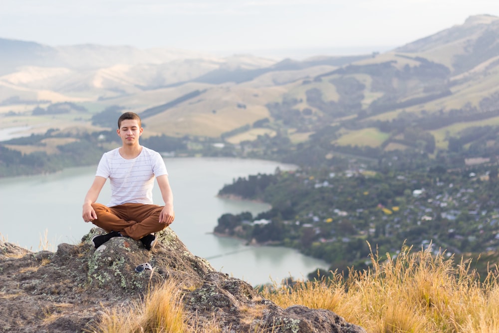 man in white crew neck t-shirt sitting on brown rock during daytime